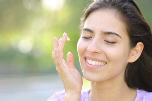 Portrait of a happy woman applying hydration cream on cheek outdoors