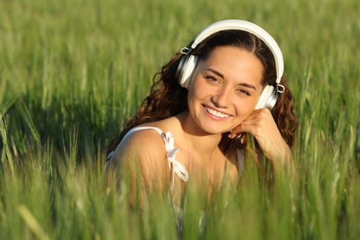 Happy woman in a green field looks at you with heaphone