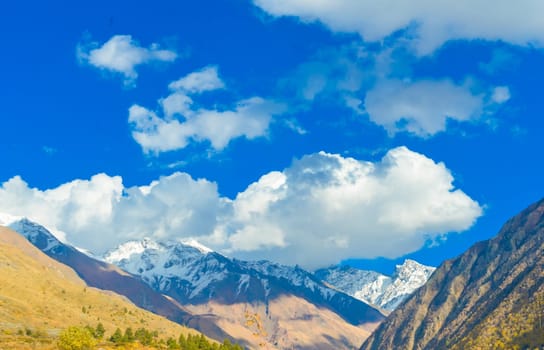Himalayan Mountain Valley in sunset sunlight against blue sky and flying clouds in the background.