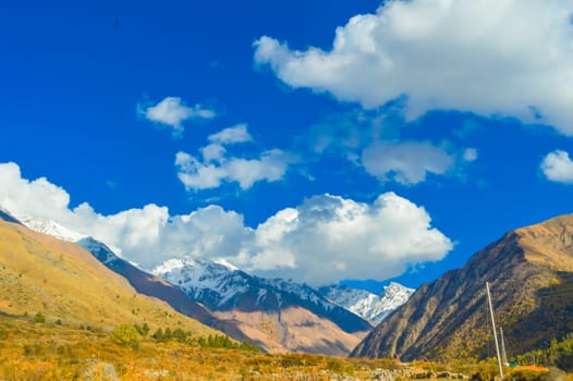 Himalayan Mountain Valley in sunset sunlight against blue sky and flying clouds in the background.