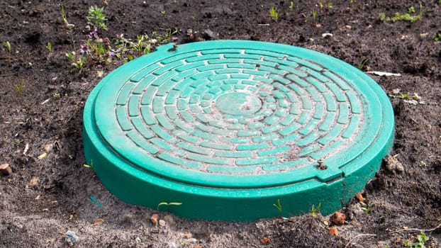 New green metal manhole on the land. Repair work. The closed sunroof does not pose a danger to pedestrians and vehicles. Underground pipeline repair