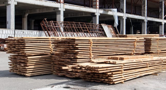 Pile of stacked wooden planks at a construction site. Wooden boards, lumber. Industrial edged timber. Wooden rafters for the repair or construction of a private house. Roofing and joinery lumber