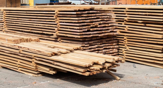 Pile of stacked wooden planks at a construction site. Wooden boards, lumber. Industrial edged timber. Wooden rafters for the repair or construction of a private house. Roofing and joinery lumber