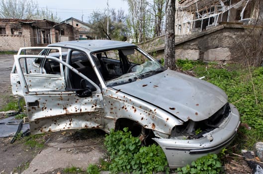The car that burned down after the bombing of the city stands in the courtyard of a destroyed house. War between Russia and Ukraine. Fragments of a car after artillery shelling