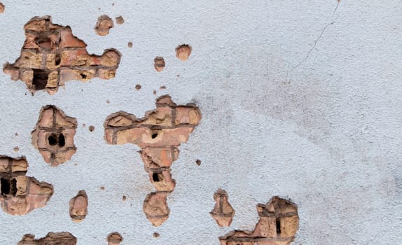 The wall of a building battered by rocket fragments in a war zone. Shelled wall. Facade of a bombed-out building. Armed conflict in Ukraine. Damage to the house as a result of artillery shelling