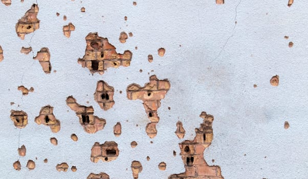 The wall of a building battered by rocket fragments in a war zone. Shelled wall. Facade of a bombed-out building. Armed conflict in Ukraine. Damage to the house as a result of artillery shelling