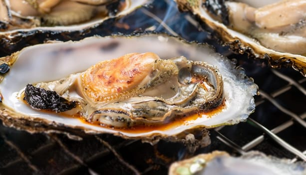 Grilling fresh hotate japanese scallops and kaki oysters in shells on barbeque grill with glowing coals, popular Otaru city street food, Japan