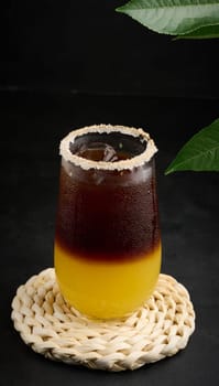 Iced coffee with orange juice in a transparent glass, refreshing bumble coffee on the table, black background