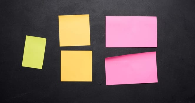 Multicolored paper stickers on a black chalkboard, space for notes and labels