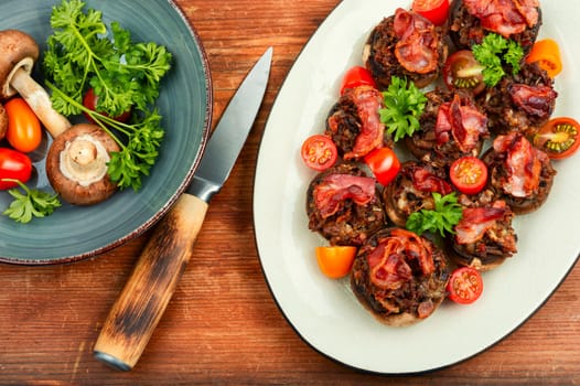 Tasty champignon mushrooms stuffed with meat, tomatoes and bacon on on rustic wooden background. Top view.