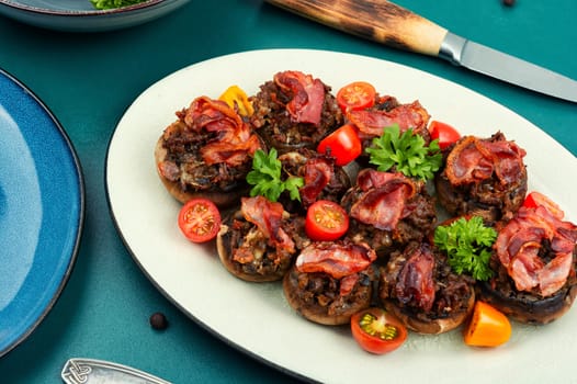 Tasty champignon mushrooms stuffed with meat, tomatoes and bacon on on rustic wooden background. Top view.