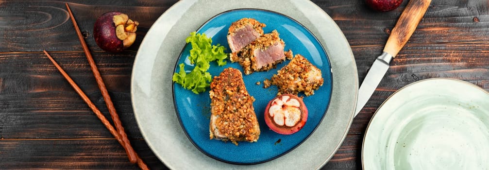 Steak of baked tuna in a nut panic with a mangosteens on rustic wooden table. Flat lay.