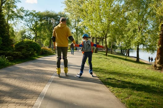Grandparent and boy roller skating together in city park. Recreational entertainment on weekend in summer