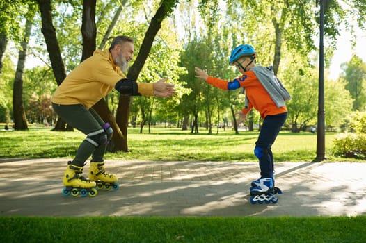 Grandfather teaching grandson riding roller skates in city park. Happy family enjoying fun time and active sport recreation outdoors