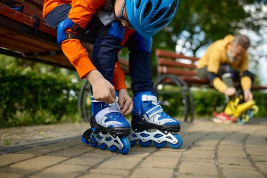 Selective focus of grandson and grandfather putting on roller skates. Mature man and boy preparing for racing in park playground