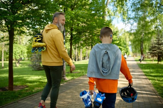 Grandfather with grandson walking in park preparing roller-skates and helmet or extreme racing