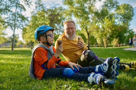 Happy grandpa and grandchild eating ice-cream after roller skating. Happy family rest in park