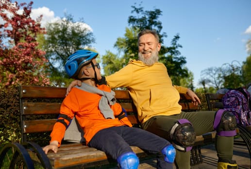Happy grandparent and grandchild rest on bench in park after speed racing on roller skates