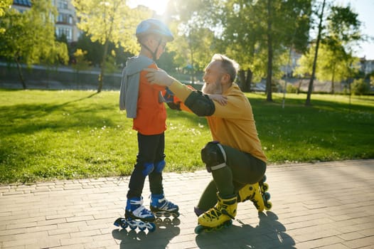 Loving grandpa supporting adorable little grandson while roller skating on city street