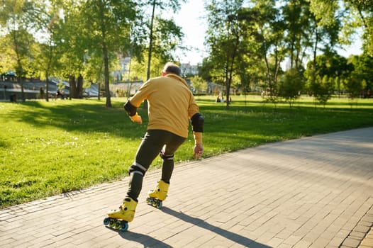 A senior man moving fast on roller skates in city park. Happy retiree learning rollerblading tricks and stunts for extreme riding