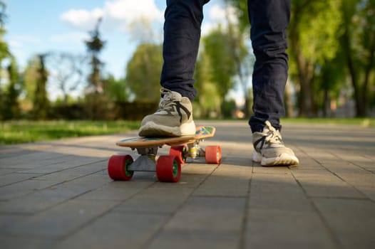 Closeup boy leg wearing trainers on skateboard over street background. Extreme skateboarding time on weekend