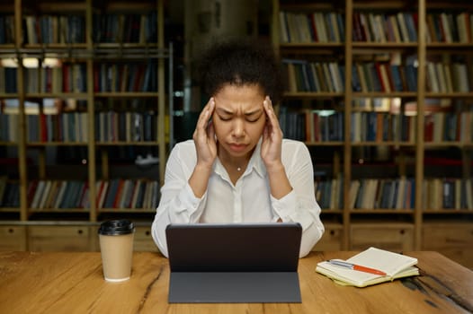 Tired overworked female office worker touching head massaging temples suffering from headache or tension while sitting at desk table front of computer