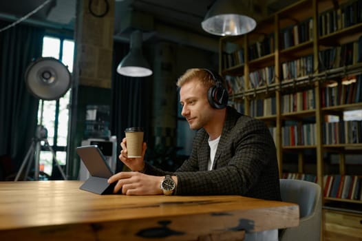 Businessman wearing headphones holding video conference with partners sitting at desk table with laptop computer in office. Online meeting, digital communication, virtual chat briefing concept