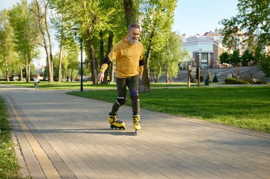 Happy mature man rollerskating on pathway in city park. Senior male feeling joy and fun during active sports recreational time on weekend