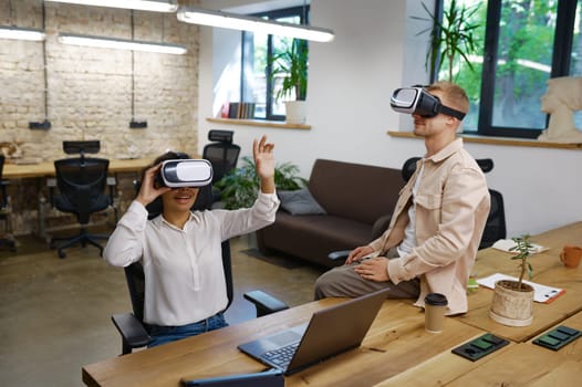 Inspired man and woman coworker wearing vr goggles in office. Male and female colleagues in virtual reality headset playing online games using cyberspace for business meeting and communication
