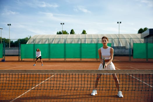 Woman and man behind net playing tennis. Sporty couple with racket enjoying double set game training