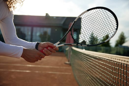 Closeup view of tennis player holding racket standing front of net. Healthy activity and sports hobby concept