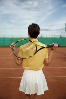 Back view on young teenage woman tennis player holding racket on shoulders. Recreational activity and professional sport concept