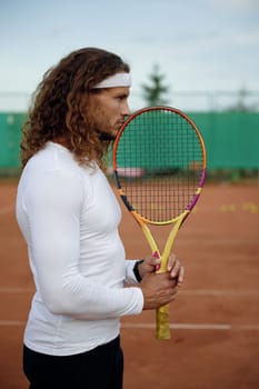 Pensive male tennis player thinking about game strategy during break time. Worried sportsman holding racket looking with belief in victory