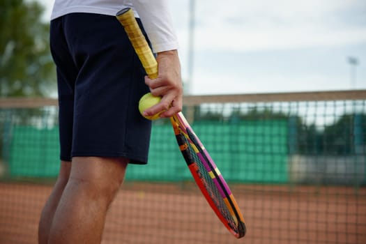 Closeup view on tennis racket and ball in hand on sportsman over outdoor sports court background. Professional competition challenge or training in fitness club