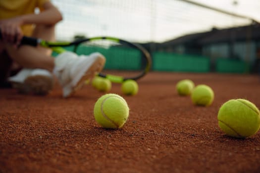 Rest after game shot with focus on balls scattered across playing field and relaxed tennis player sitting on floor
