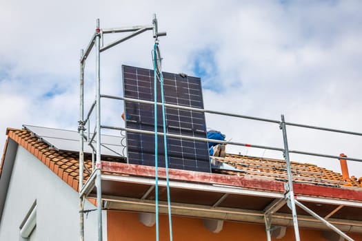 Lifting solar panels using pulley. Installing solar panels on a roof. Solar panels on roof. Workers installing solar cells.