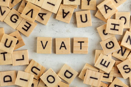 Top down view, pile of square wooden blocks with letters VAT (stands for Value added tax) on white board.