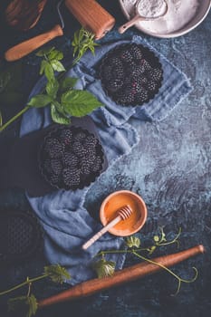 Organic blackberries in baking forms, ripe blackberries with baking ingredients and kitchen untensil