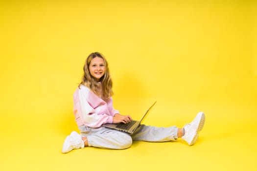 Positive kid sit with a laptop read homework wear casual style cloth isolated over yellow background