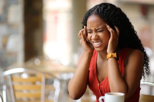 Black woman suffering migraine sitting in a coffee shop terrace