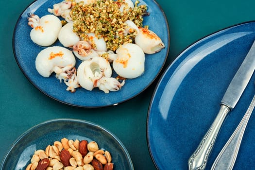 Baked young squids served with nut salad on wooden table.