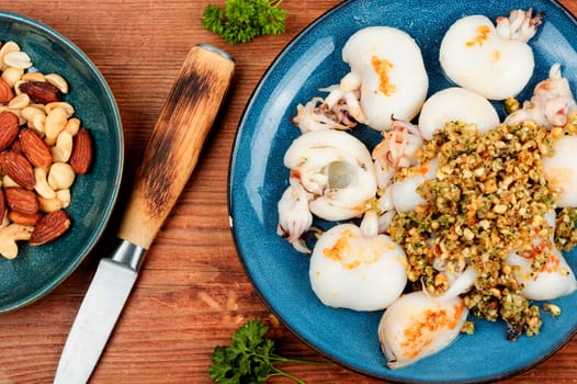 Baked young squids served with nut salad on wooden table.