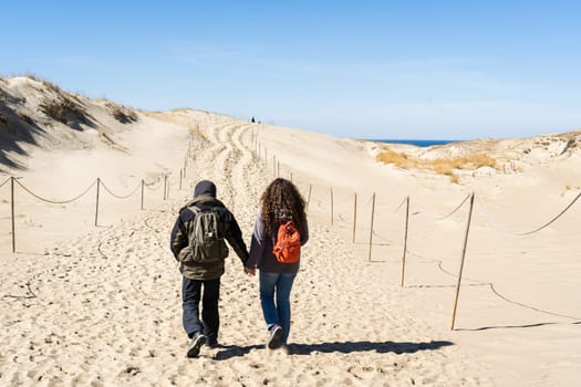 A couple of backpackers hand in hand walk along the hilly sand dunes on the Curonian Spit, Lithuania.