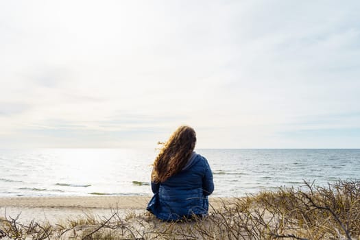 Long-haired curly plus size woman on the seashore, rear view.