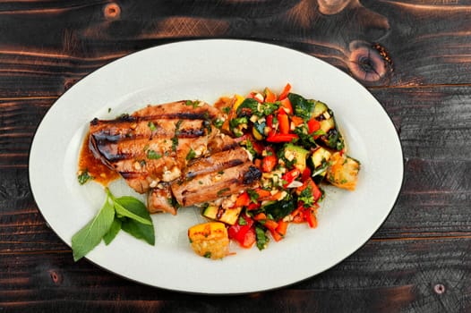 Delicious grilled tuna steak with baked vegetables on a plate.
