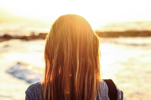 Young woman watches over sea during sunset. View from back, detail on only her hairs.