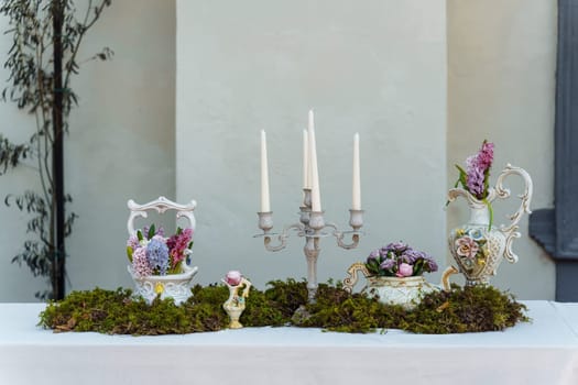 Decorative decoration of the festive table. Candlestick with candles, vases with hyacinths and other flowers, green moss on a table covered with a white tablecloth.