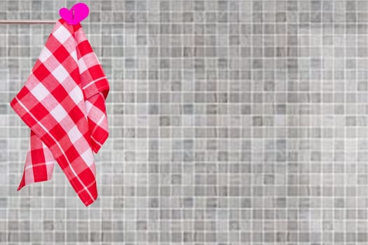 A red checked kitchen towel hanging on a clothes rail against abstract blurred beige gray mosaic ceramic tile wall. Space for your product display montage.