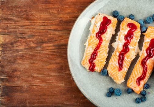 Roasted salmon fillet with blueberry berry sauce on ceramic plate.
