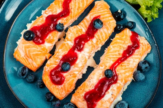 Roasted salmon fillet with blueberry berry sauce on ceramic plate.